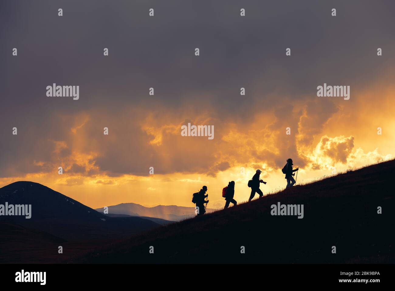 Group of unrecognizable hikers are walking at majestic sunset in mountains Stock Photo