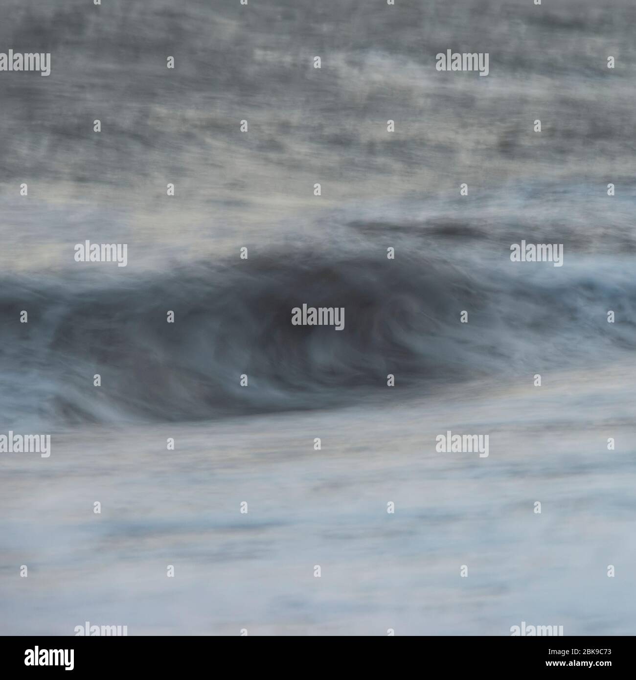 Beautiful abstract long exposure landscape image of waves crashing onto groynes on beach during sunset Stock Photo