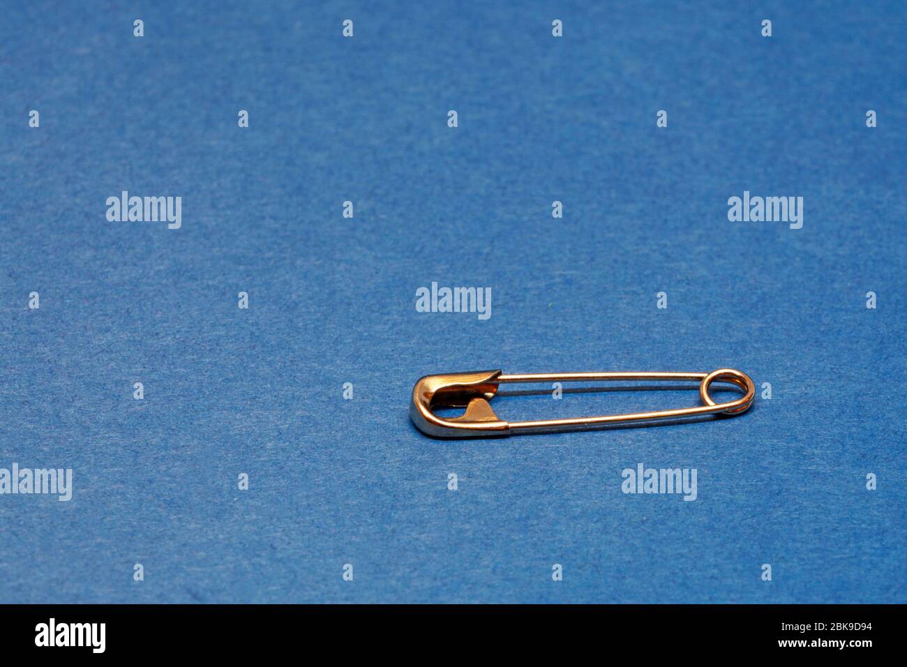 safety pin in gold on blue background Stock Photo Alamy