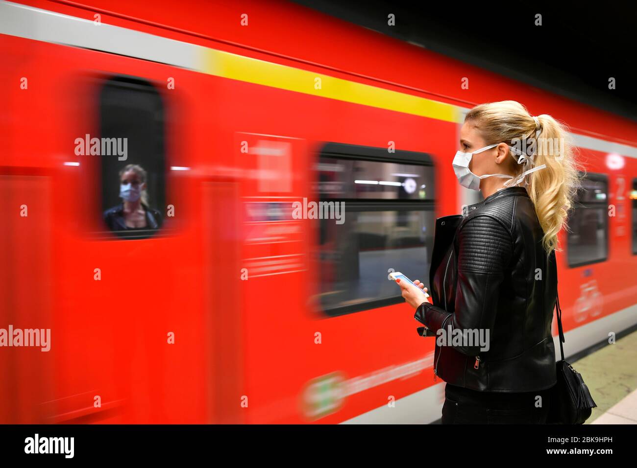Woman with face mask, on mobile phone, waiting for train, S-Bahn, reflection in window, corona crisis, Stuttgart, Baden-Wuerttemberg, Germany Stock Photo
