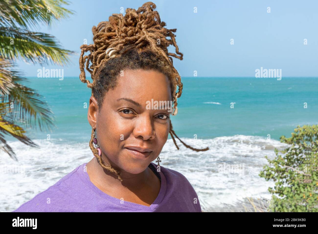 Close Up Portrait of Beautiful Black, African, or Carribean woman looking serious outdoors overlooking gorgeous beach and ocean. Stock Photo