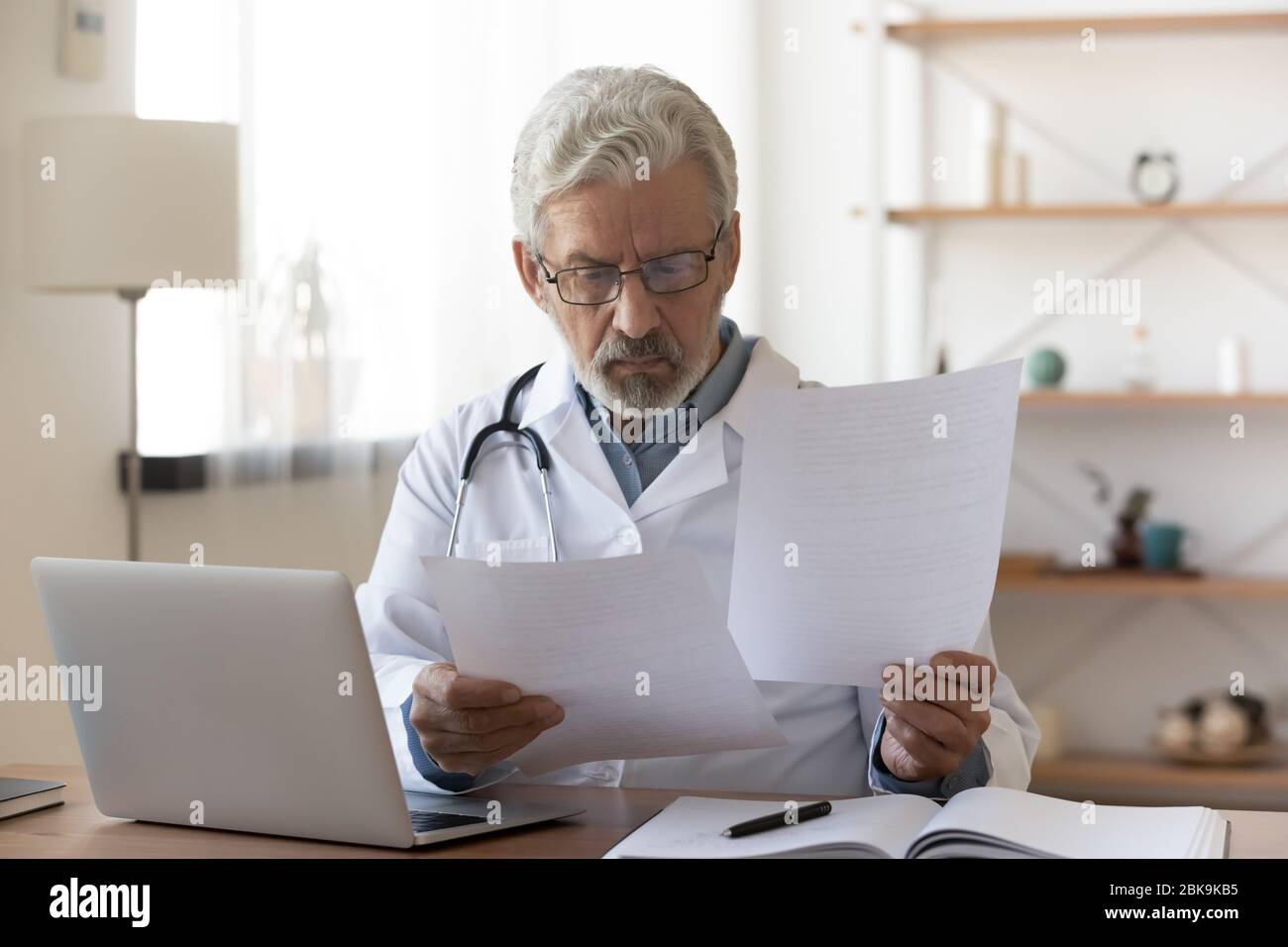 Serious professional senior doctor checking medical documents at workplace Stock Photo