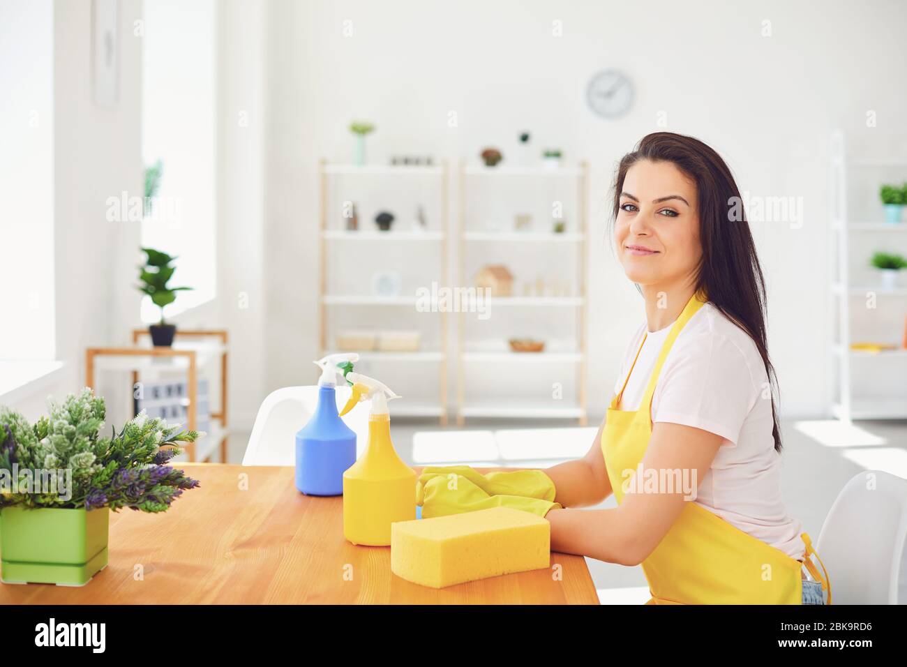 Happy young woman cleans the room in the house. Girl wash in gloves while sitting on the floor smiling joyful. Stock Photo