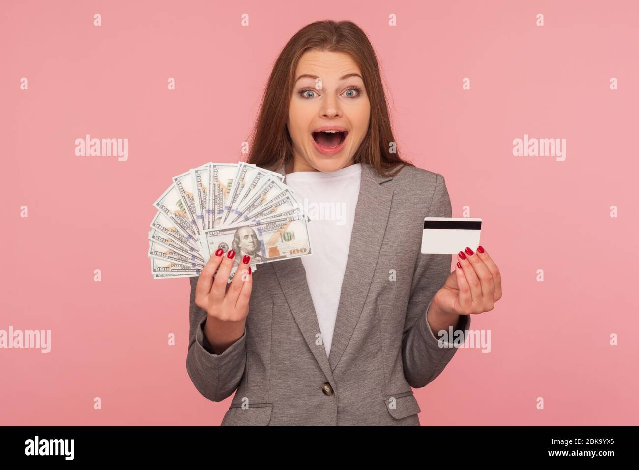 Wow, unbelievable loan, cash deposits. Portrait of surprised businesswoman in suit jacket holding dollar banknotes and credit card, shocked by amazing Stock Photo