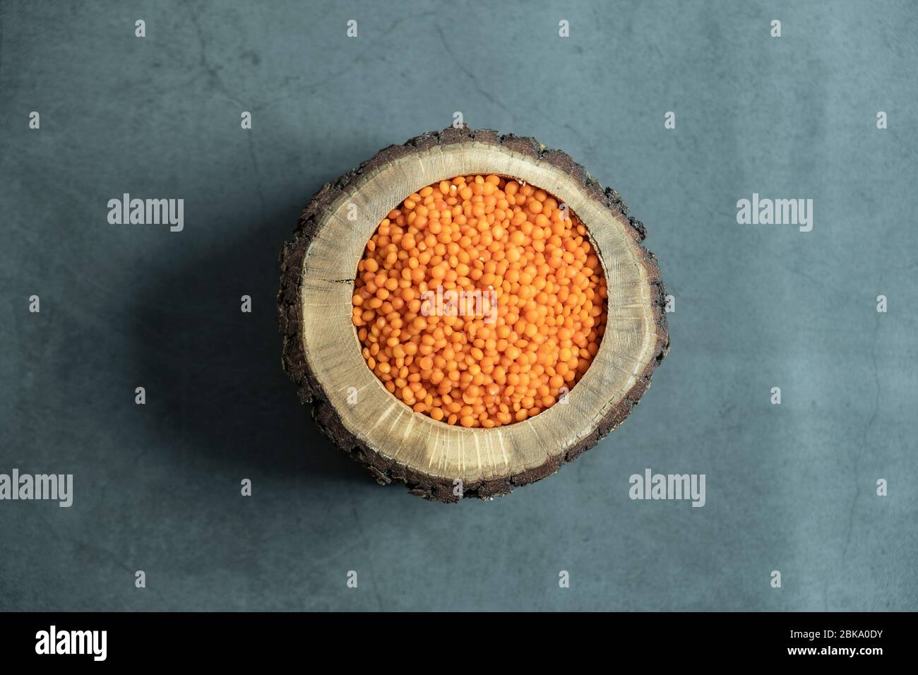 Red lentil in wooden bowl on stone, concrete background. Healthy, organic and delicious raw cereal. Top view, flat lay. Stock Photo