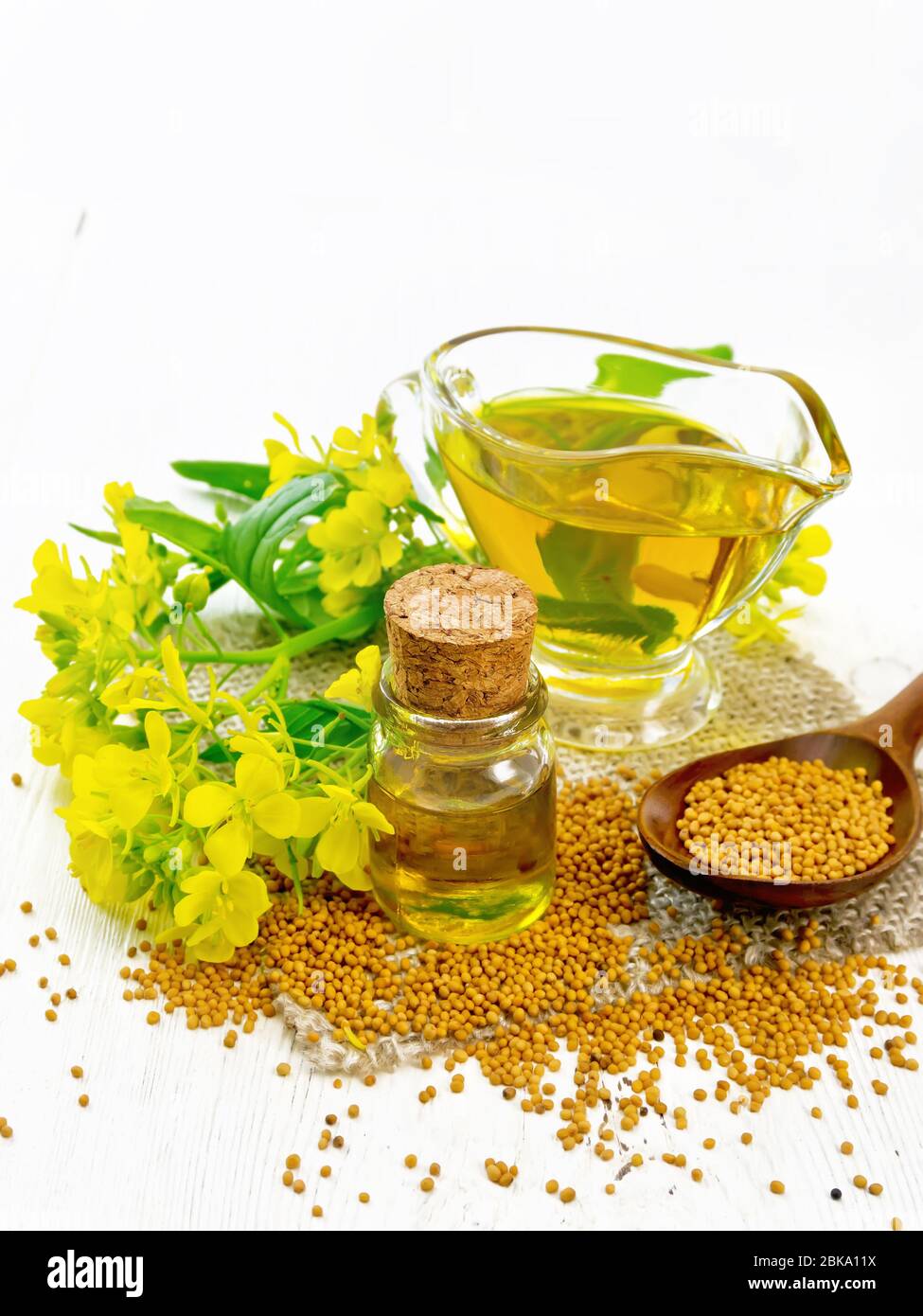 Mustard oil in a glass bottle and gravy boat, grains in a spoon and burlap,  yellow mustard flowers on wooden board background Stock Photo - Alamy