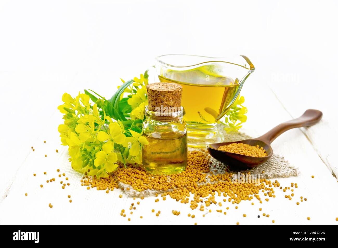 Mustard oil in a glass bottle and gravy boat, grains in a spoon and on a  burlap napkin, yellow mustard flowers on wooden board background Stock  Photo - Alamy