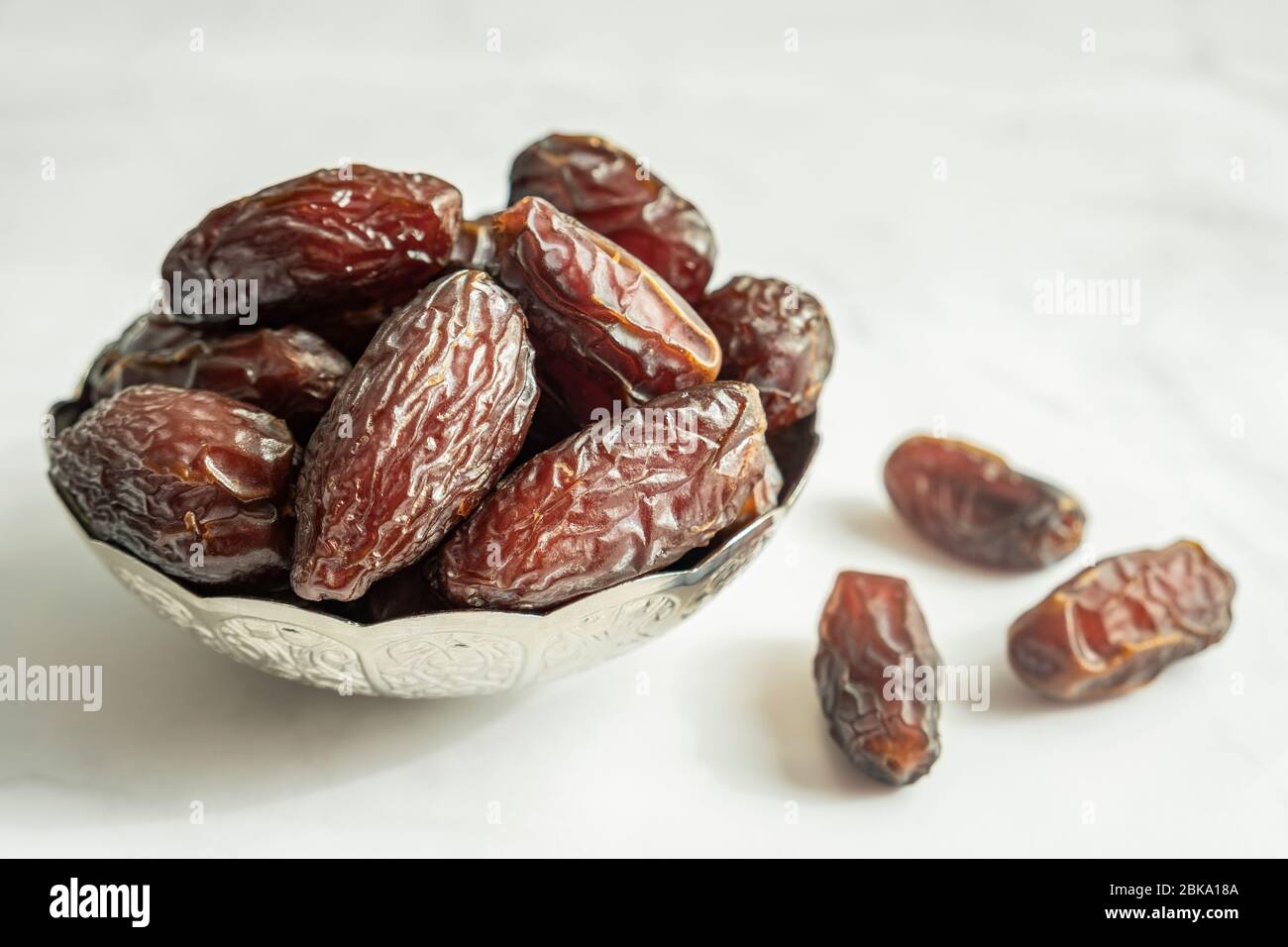 Raw date fruit ready to eat in silver bowl on a white marble background. Traditional, delicious and healthy ramadan food. Stock Photo