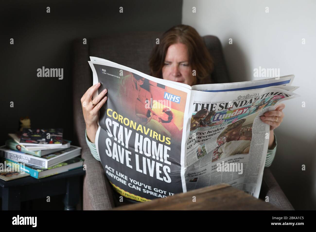 A woman reading the Sunday Times Newspaper at home during Lockdown due to the Coronavirus Pandemic sweeping the world. Stock Photo