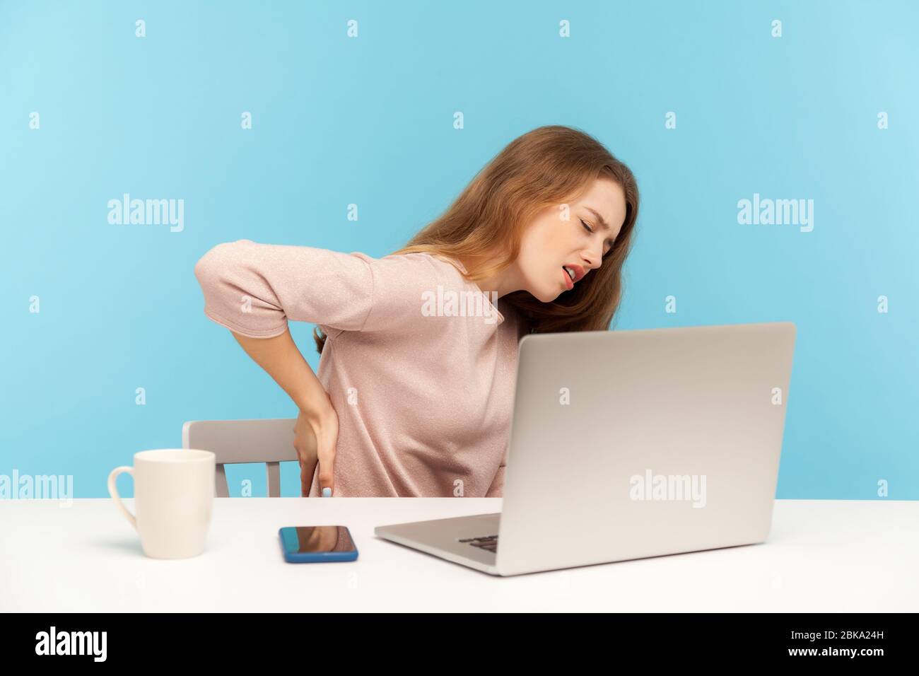 Fatigued unhealthy woman, office employee, sitting at workplace feeling unwell with sore back, hurting stiff muscles and spasms from sedentary lifesty Stock Photo