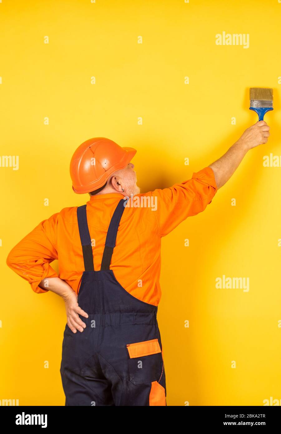 painting yellow wall. painter in working uniform working indoor. man