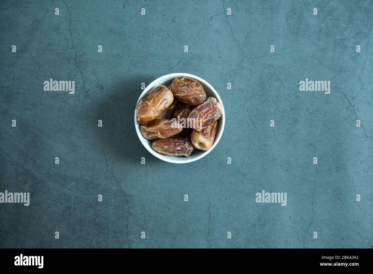 Raw date fruit ready to eat in porcelain bowl on concrete background. Traditional, delicious and healthy ramadan food. Top view, flat lay. Stock Photo