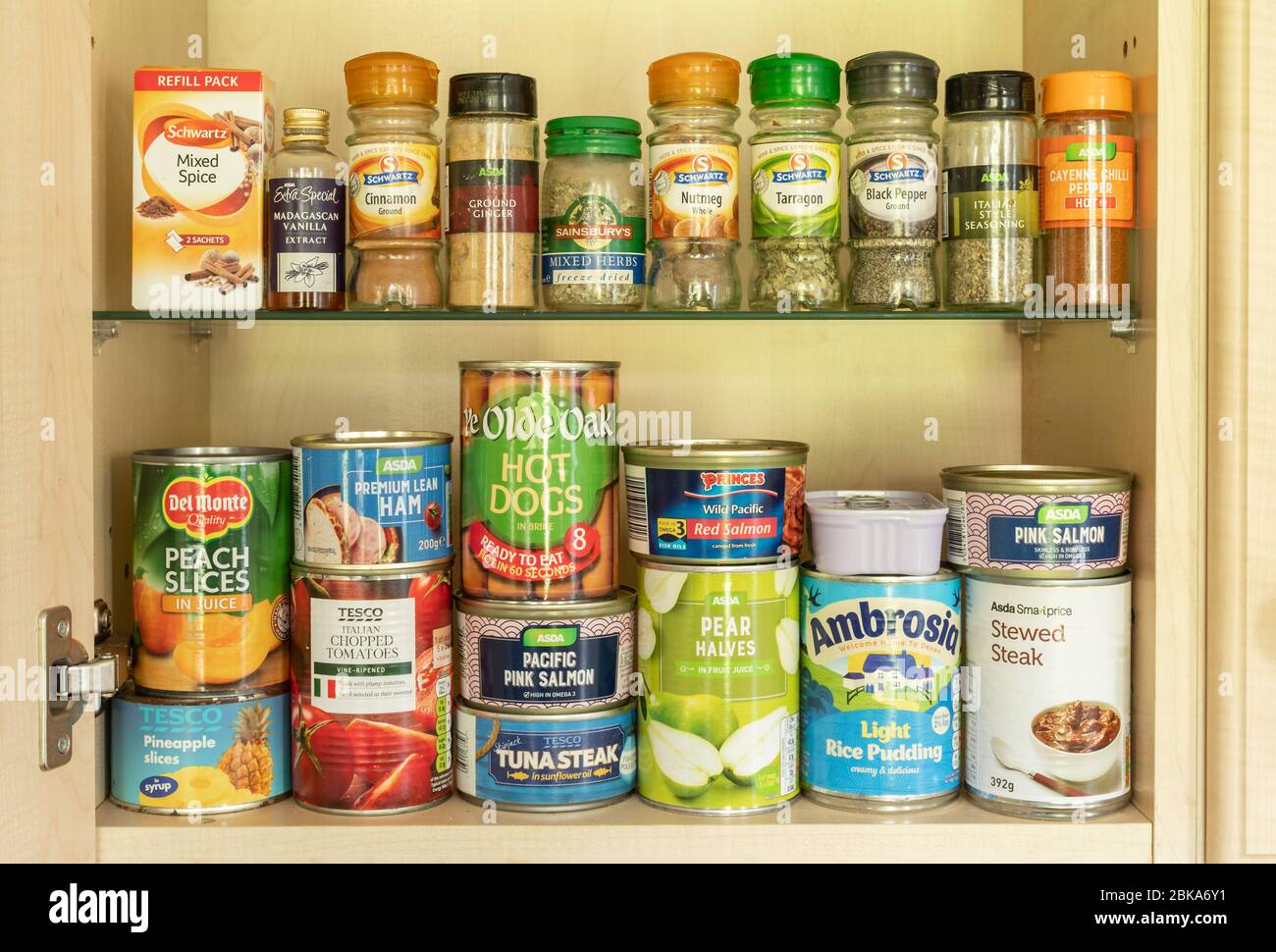 Tinned food (canned food) in a kitchen store cupboard. Tins, cans, jars of herbs and spices Stock Photo