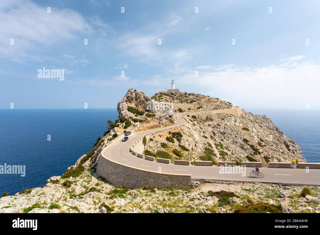A cyclist on a road heading towards a lighthouse at the tip of Cap de Formentor, Mallorca, Spain Stock Photo