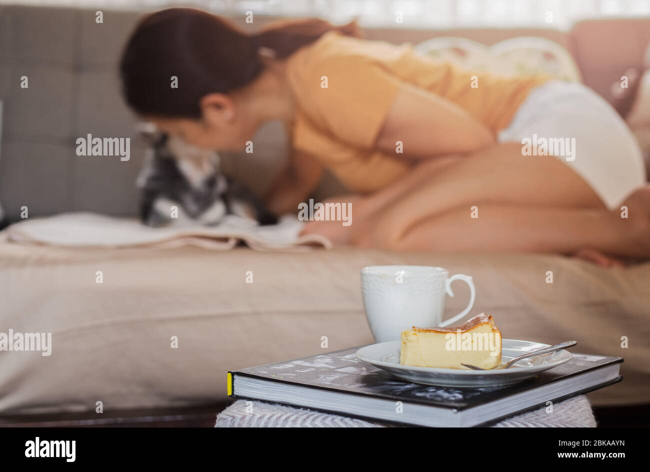 Relaxing woman kissing her dog on sofe with basque burnt cheesecake and coffee on the table Stock Photo