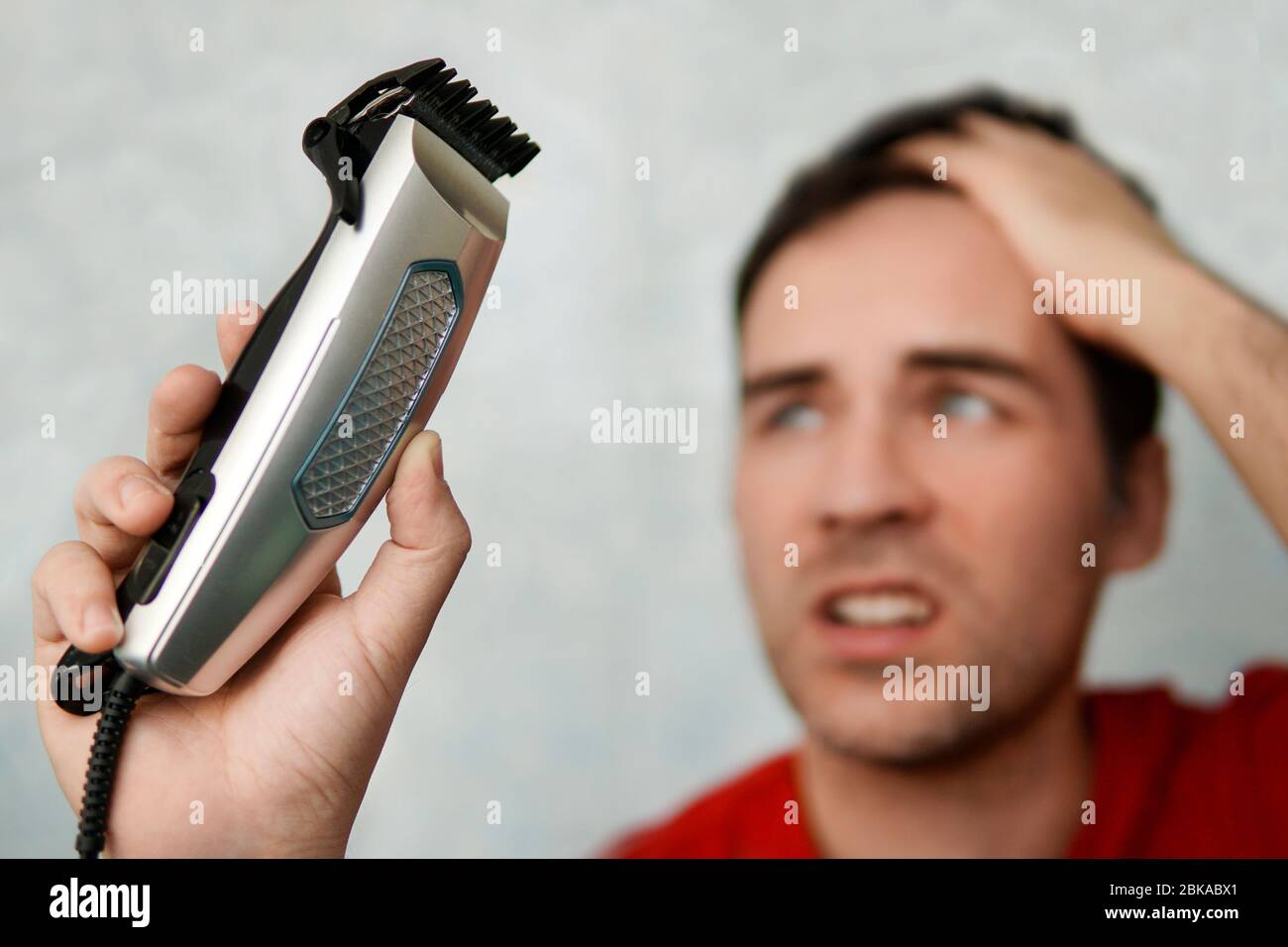 Handsome man cutting his own hair with a clipper and looks in the