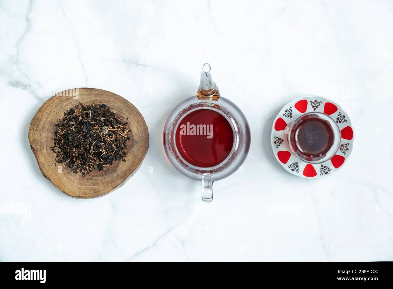 Dry black tea leaf in wooden platter and traditional Turkish tea glass with a teapot on marble