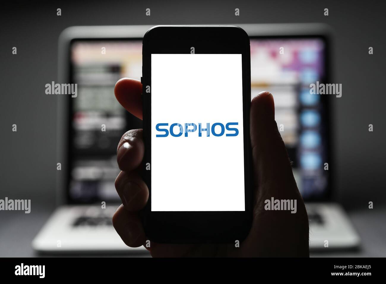 A man looking at the logo for Sophos on his iphone. Sophos is a cyber-security software development company. (Editorial Use Only) Stock Photo