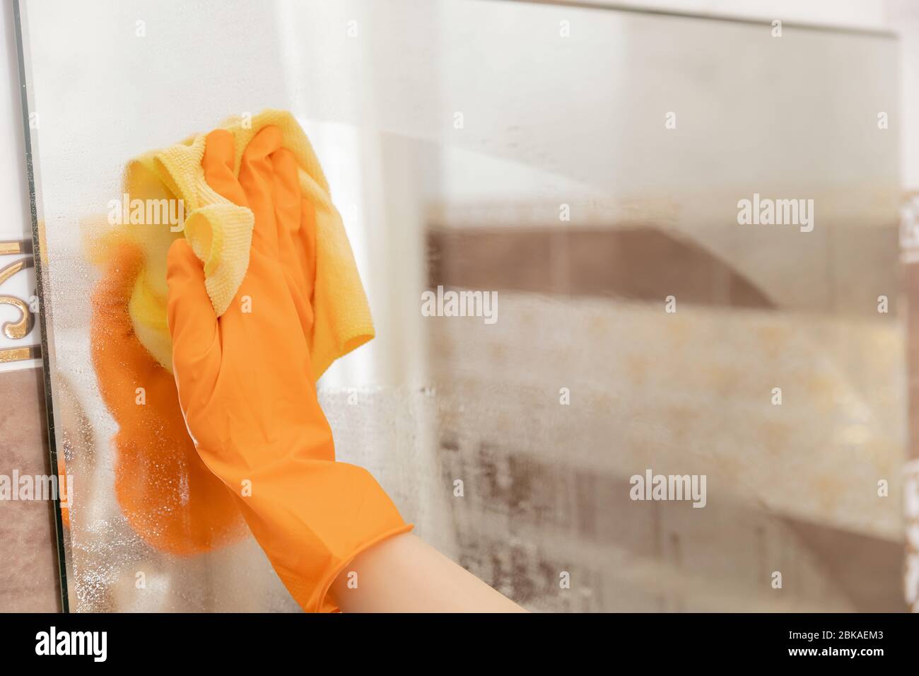 Woman cleans mirror from pollution and plaque from water in bathroom