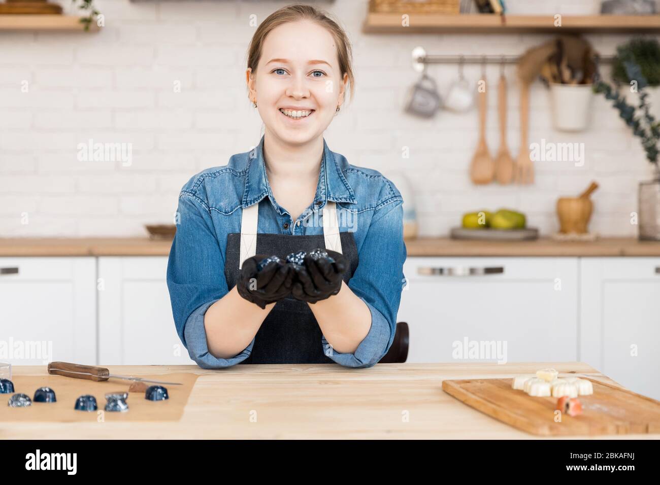 Confectioner holds sweet Belgian chocolate candies on kitchen background. Small business home concept Stock Photo