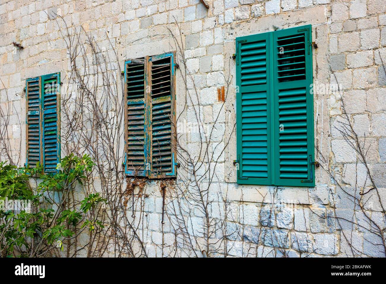 Authentic house with a stone wall, with beautiful old open windows and with green shutters, and with vases on the window. Montenegro Stock Photo