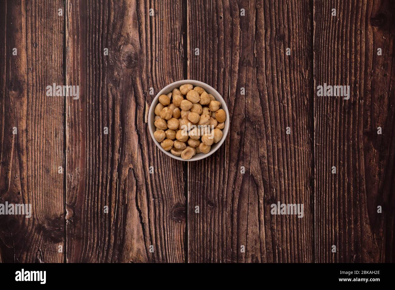 Raw hazelnut on old wooden table. Unroasted hazelnuts in white bowl and scattered hazelnuts around. Stock Photo