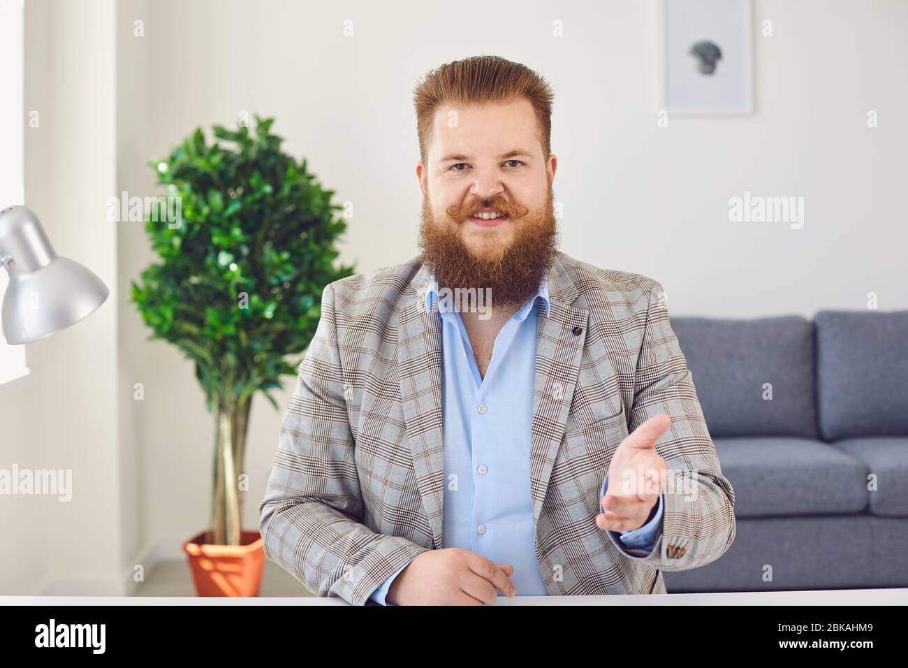 Fat man with a beard looks at the camera talking online using a webcam video chat conference sitting at home office. Stock Photo