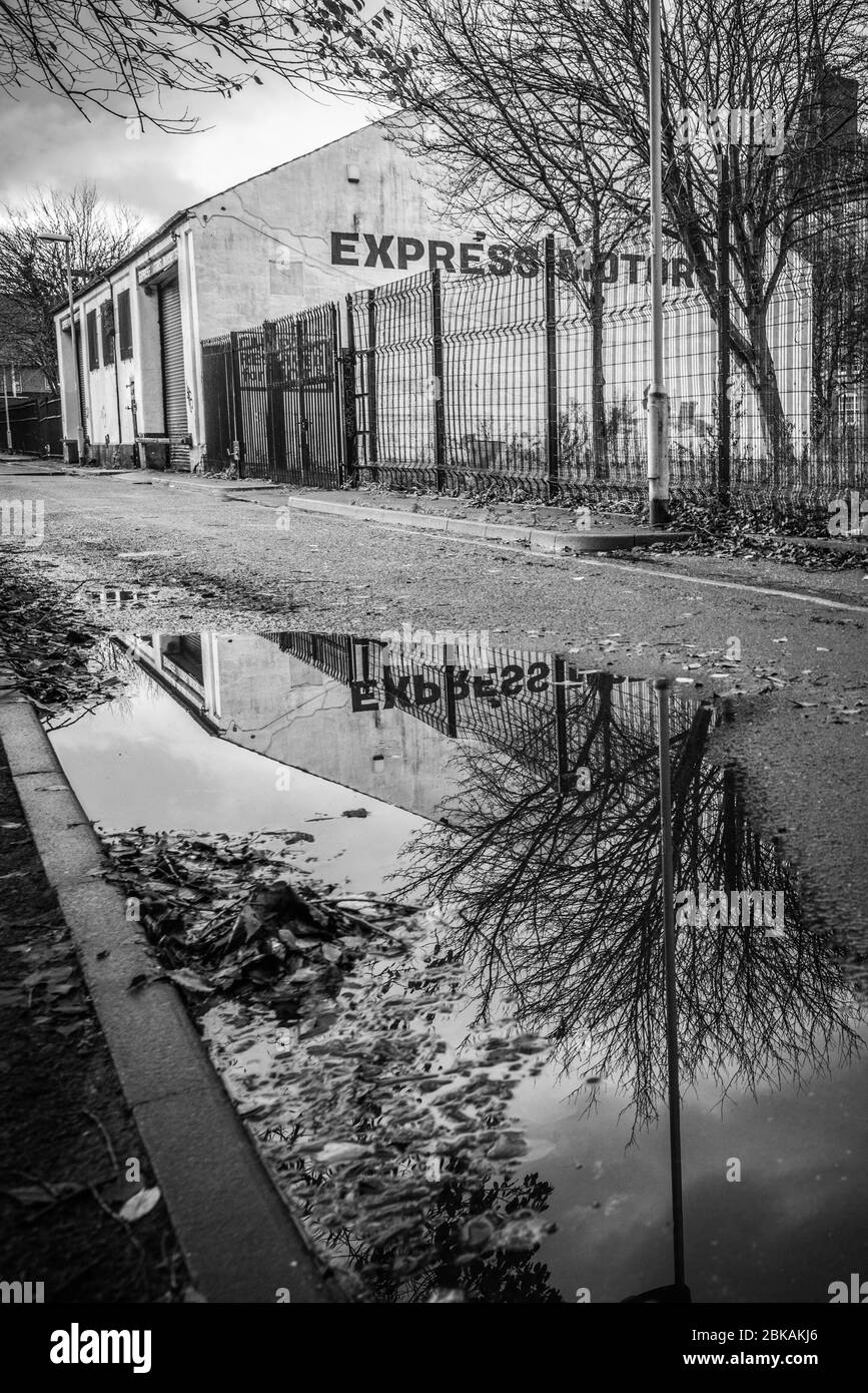 A view of a disused garage in the post-industrial district of Ancoats, central Manchester, reflected in a large puddle on a cobbled street. Stock Photo