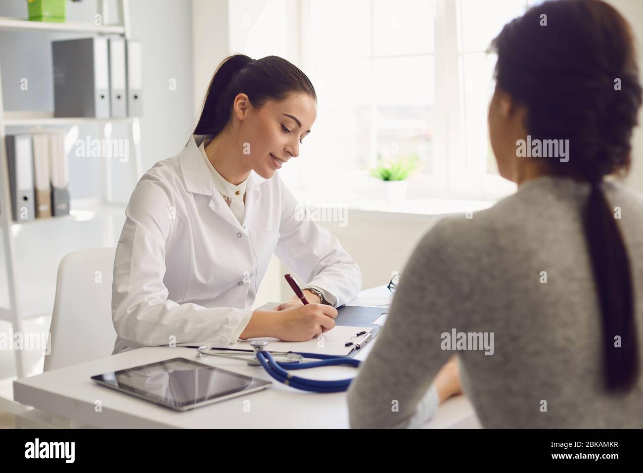 Woman patient visiting female doctor at clinic office. Medical work writes a prescription on a table in a hospital. Stock Photo