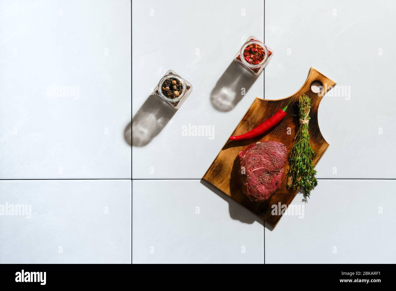 Top view of marinated raw beef steak with spice on ceramic tile with harsh shadow Stock Photo