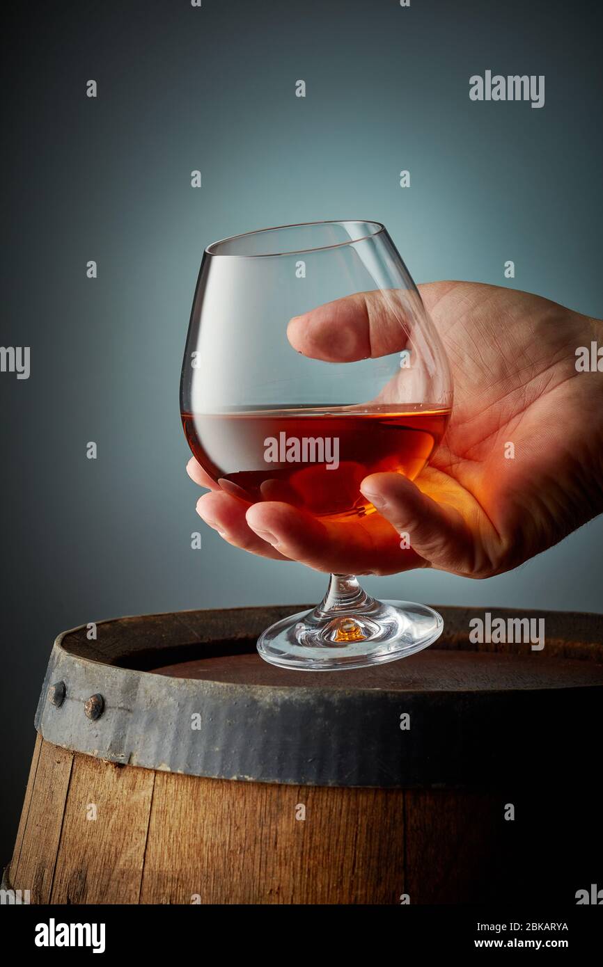 glass of cognac in human hand on grey background Stock Photo