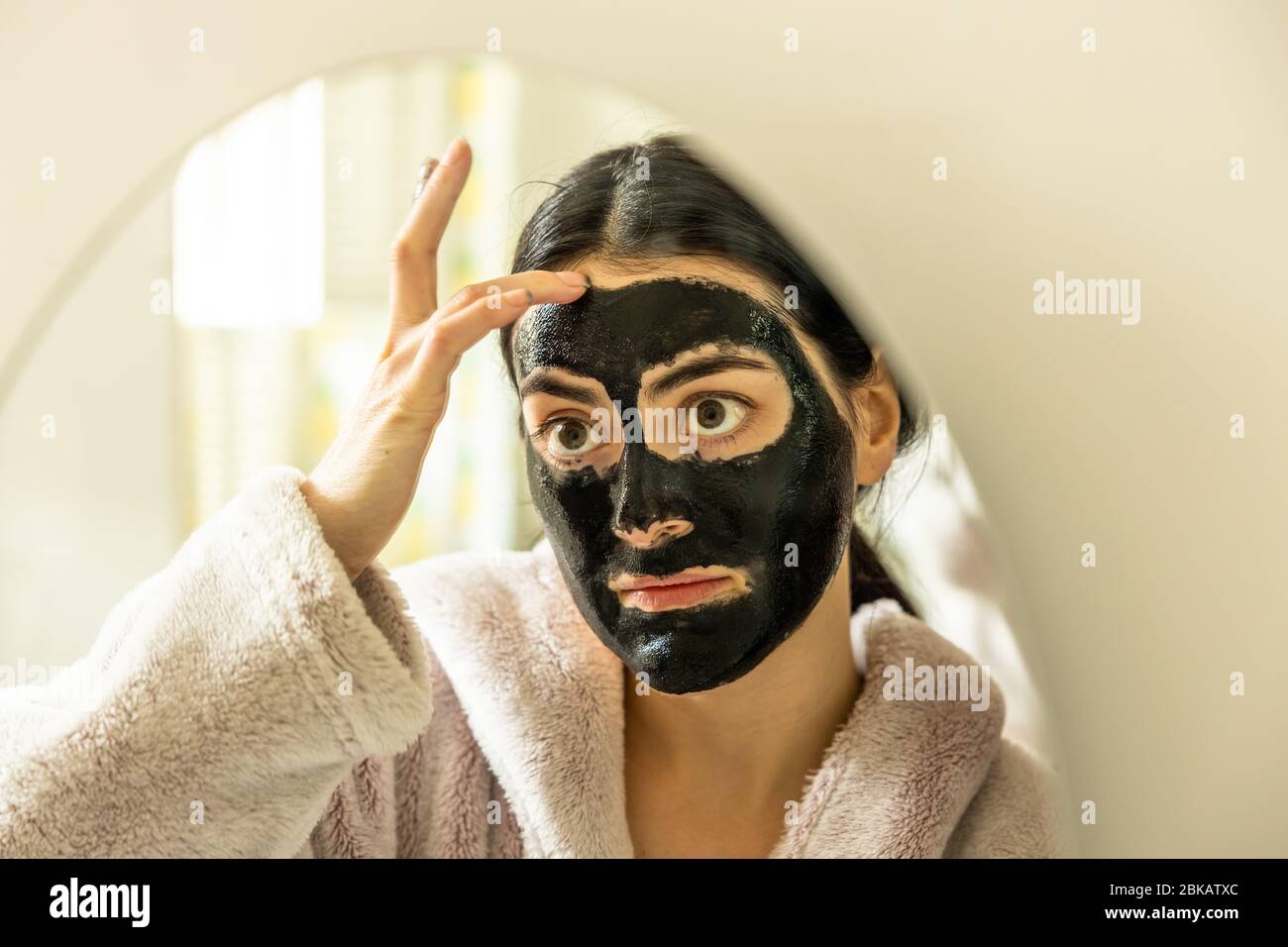 A Young millennial woman female applying a detox black charcoal peel off face mask beauty treatment in home bathroom London England UK Stock Photo