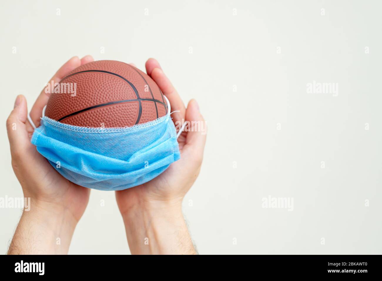 Basketball ball with medical mask in man hands on white background. Stock Photo