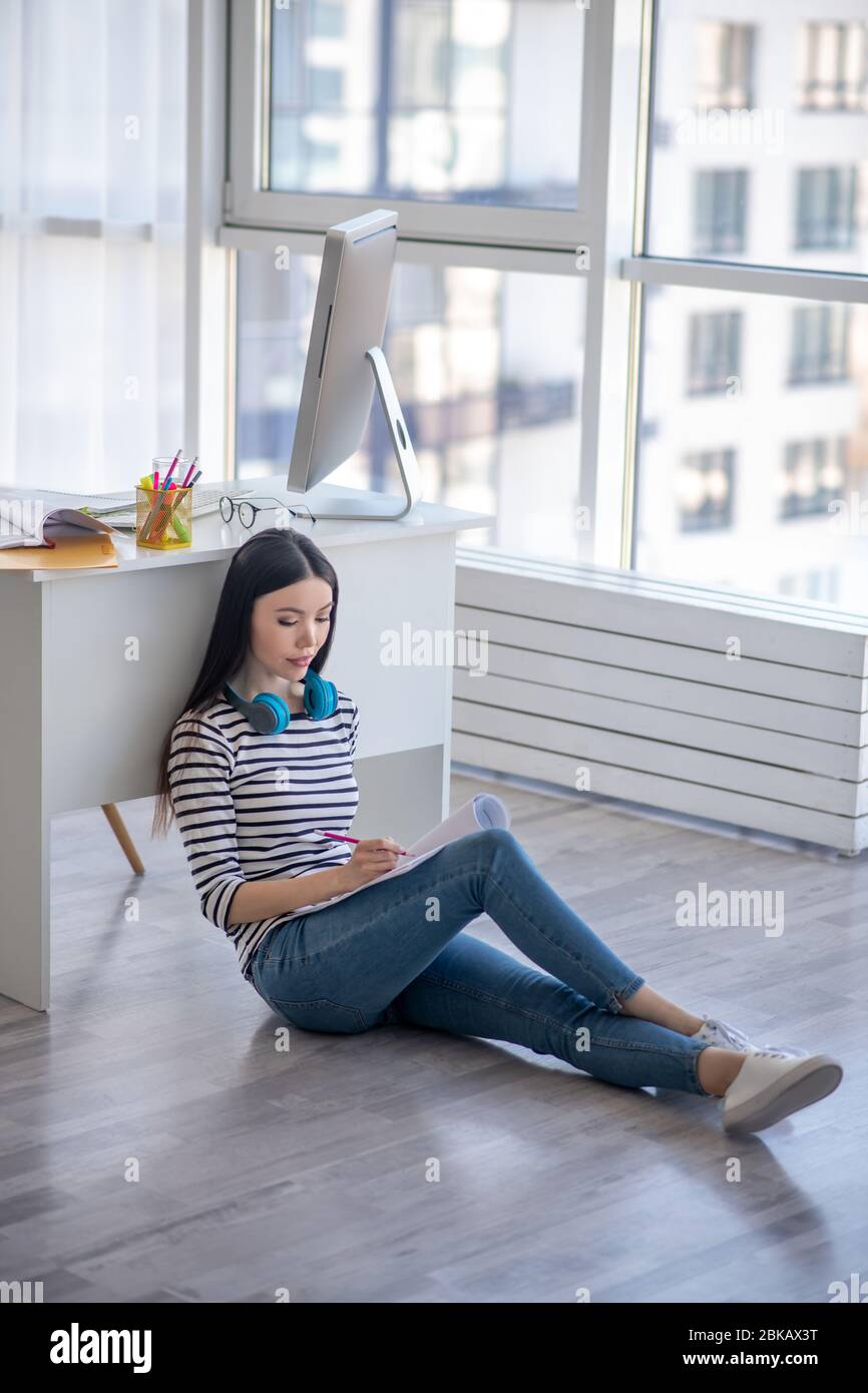 Dark-haired girl with earphones making notes in her notebook Stock Photo