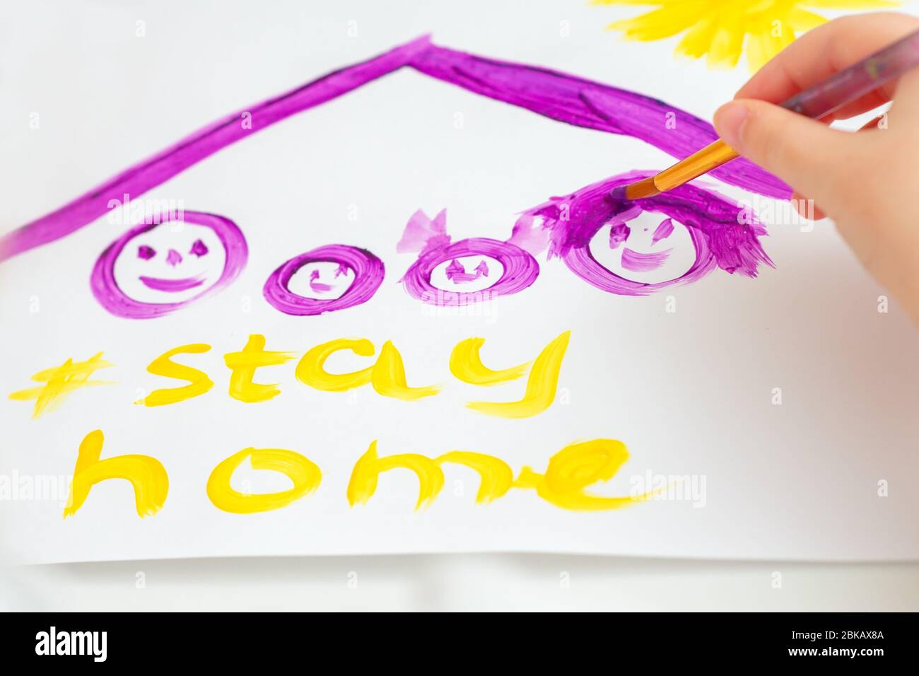 Child is drawing family under a roof with words Stay Home on sheet of paper. Children creativity. Stock Photo