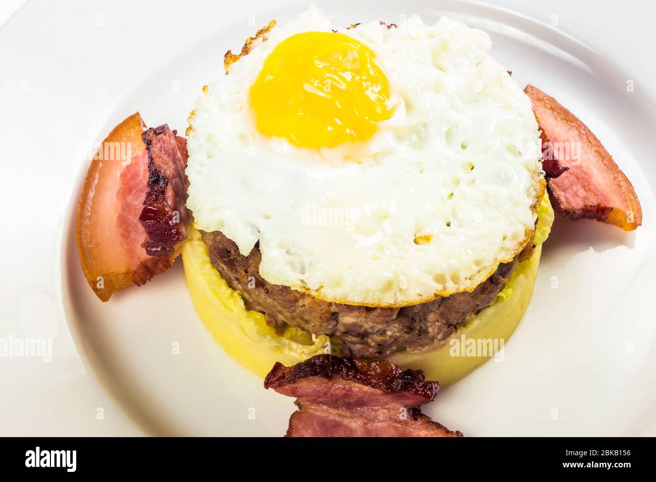 healthy homemade breakfast. fried egg and meat patty on top of smashed potato, decorated with bacon. food isolated on the white background. close up v Stock Photo