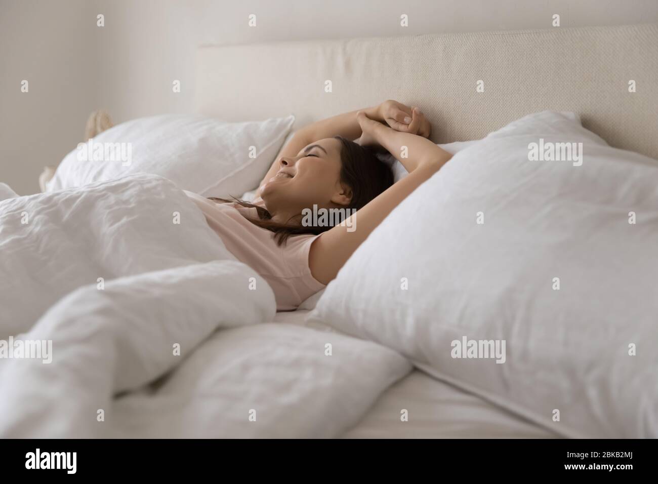Happy young woman stretch waking up in comfortable bed Stock Photo