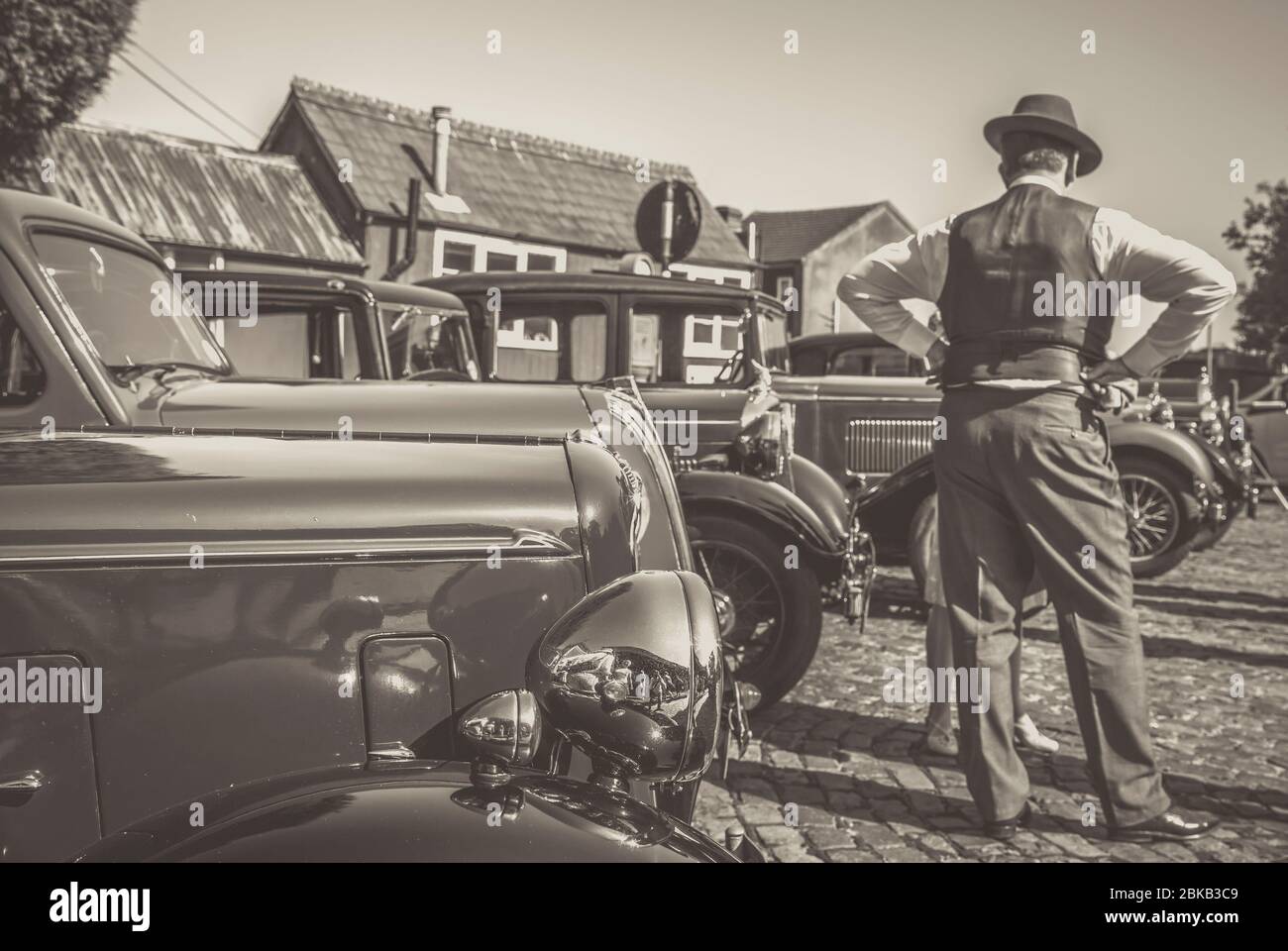 Monochrome rear view of 1940 man with vintage classic cars parked at Severn Valley Railway heritage station, 1940s WW2 wartime summer event, UK. Stock Photo
