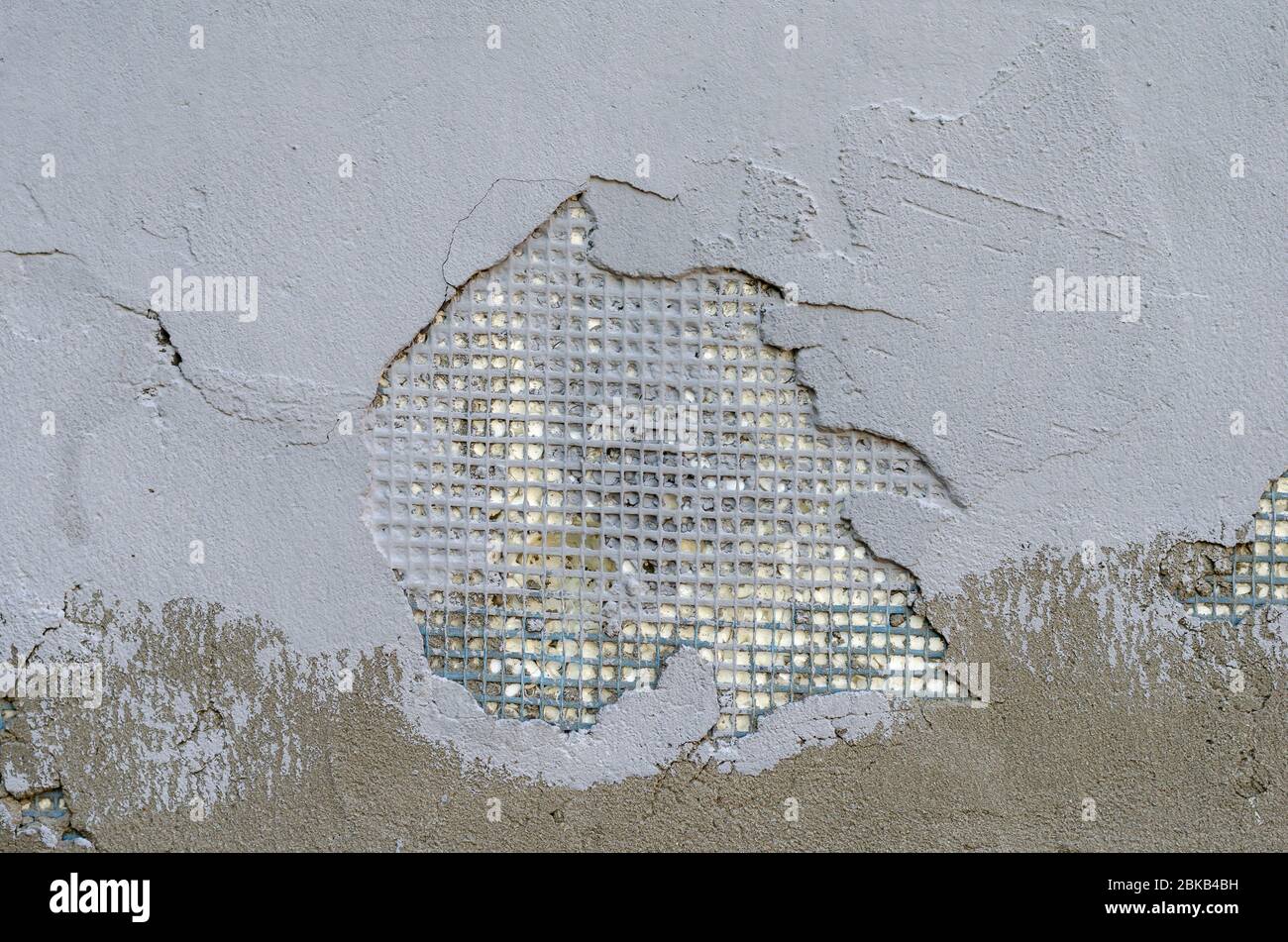 Exterior wall of a building with damaged stucco. Demonstration of poor-quality insulation of buildings. Thin layer of plaster and reinforcing mesh. Co Stock Photo