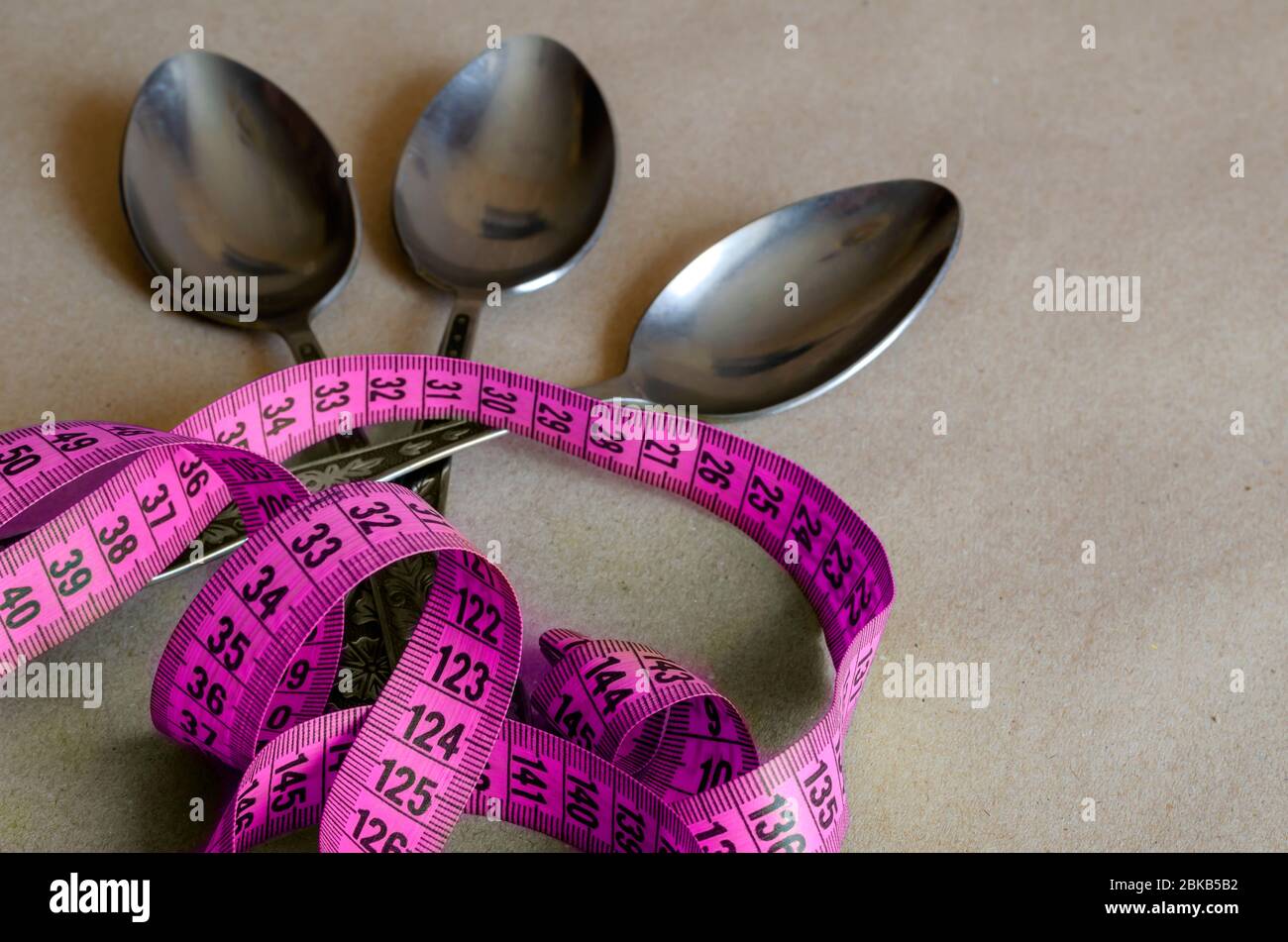 https://c8.alamy.com/comp/2BKB5B2/tailor-meter-and-three-tablespoons-measuring-tape-on-top-of-three-metal-soup-spoons-the-concept-of-overeating-during-psychological-problems-selec-2BKB5B2.jpg