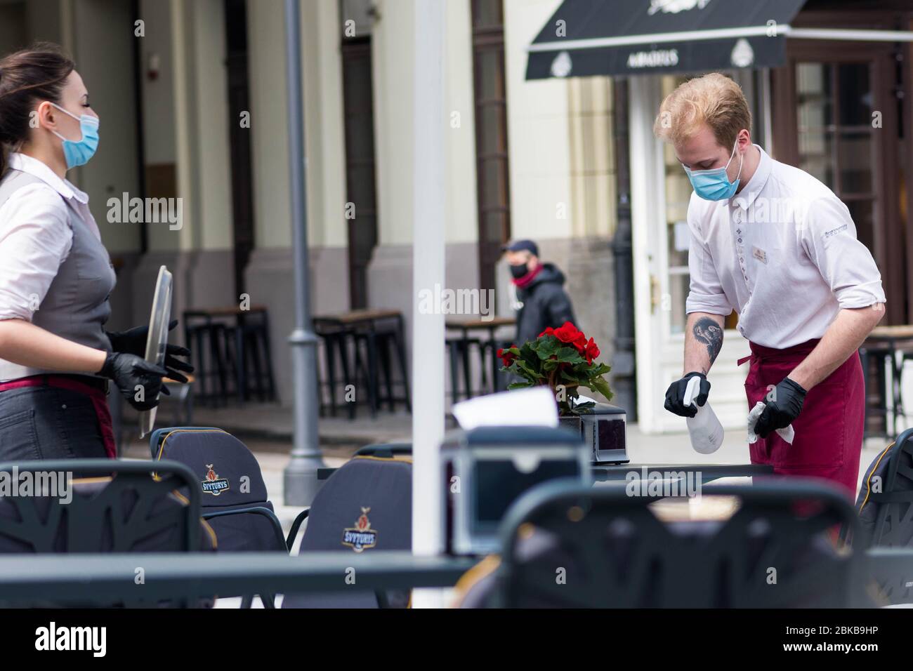 Waiter and waitress with a mask disinfecting the table of an outdoor bar, café or restaurant, reopen after quarantine restrictions Stock Photo
