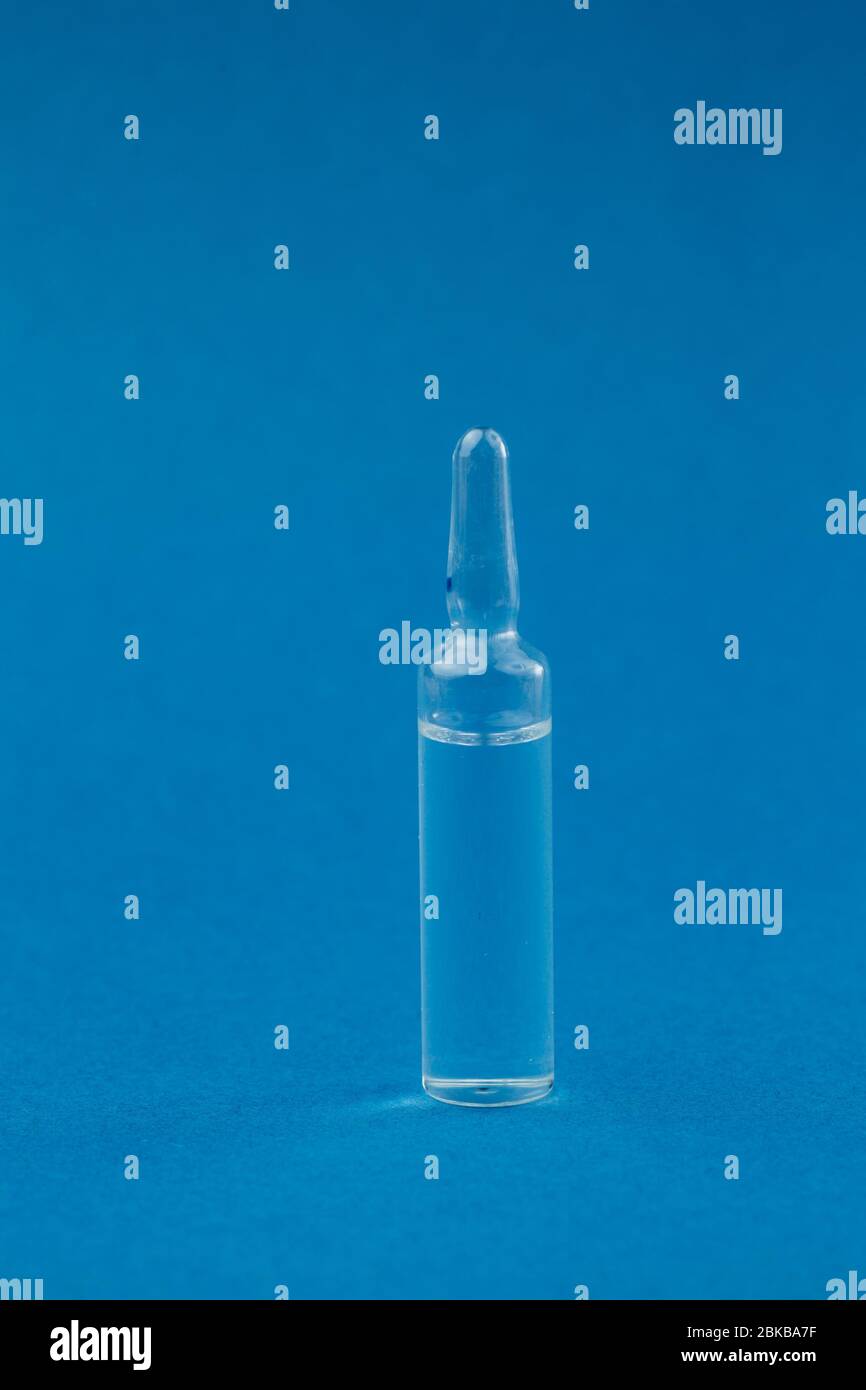 Single transparent glass ampoule with medicine on a blue background. The concept of the fight against coronavirus. Stock Photo