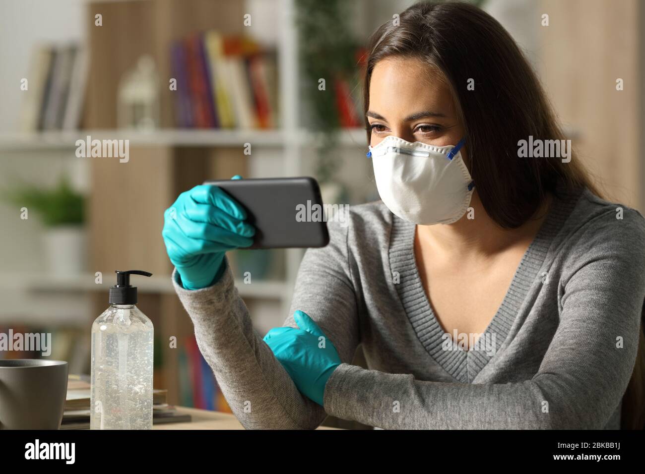Woman watching video on smart phone on coronavirus confinement itting on a desk in the night at home Stock Photo