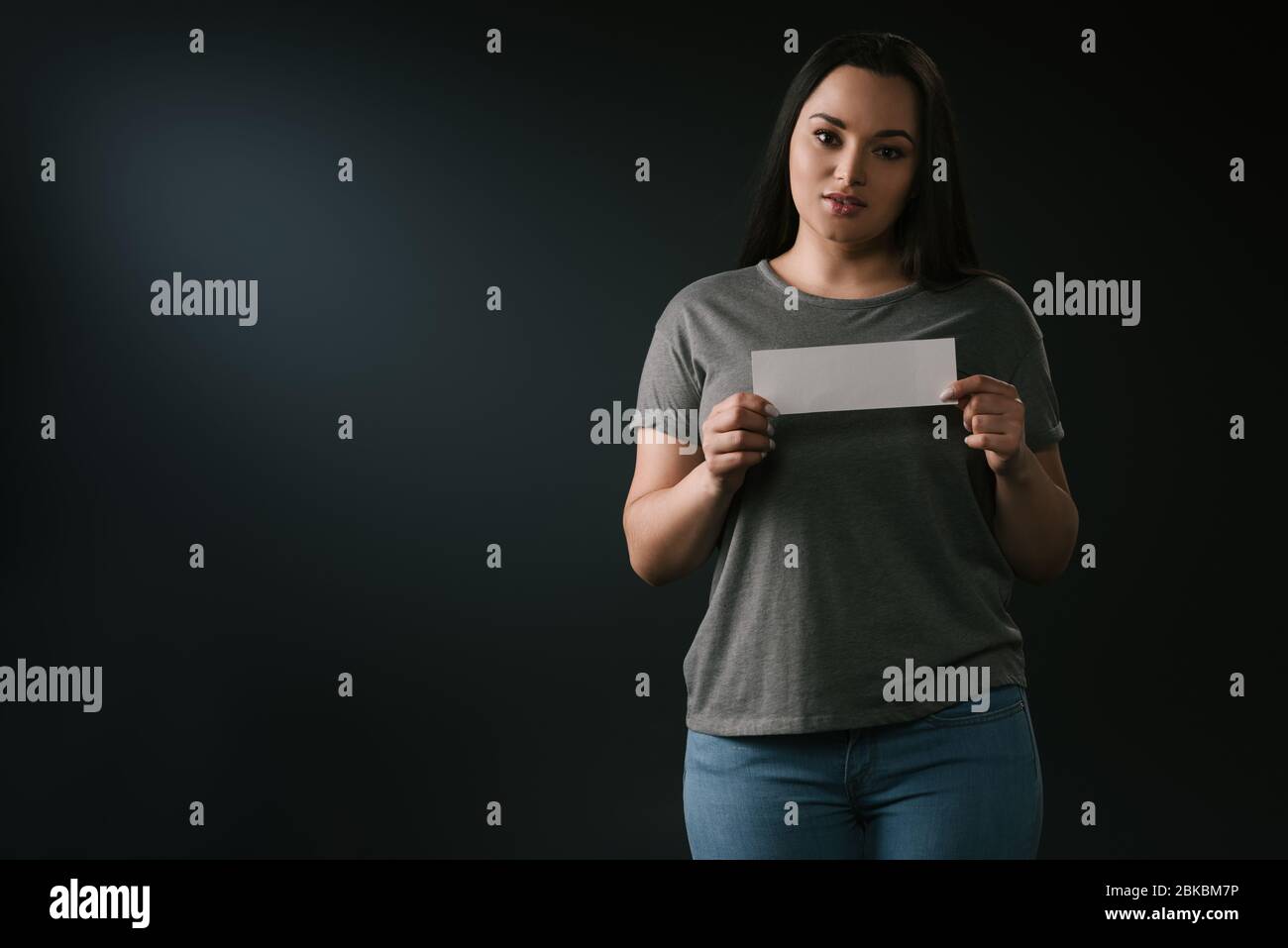 Front view of plus size attractive girl holding empty card on black background Stock Photo