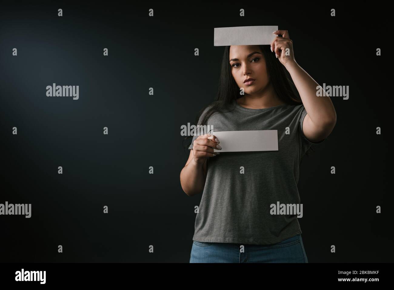 Front view of pretty plus size girl holding empty cards for copy space on black background Stock Photo