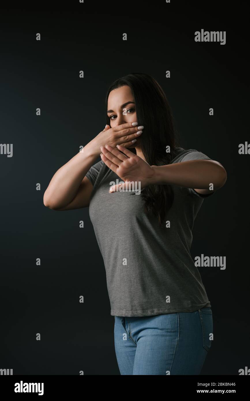 Plus size girl expressing silence with stop gesture isolated on black Stock Photo