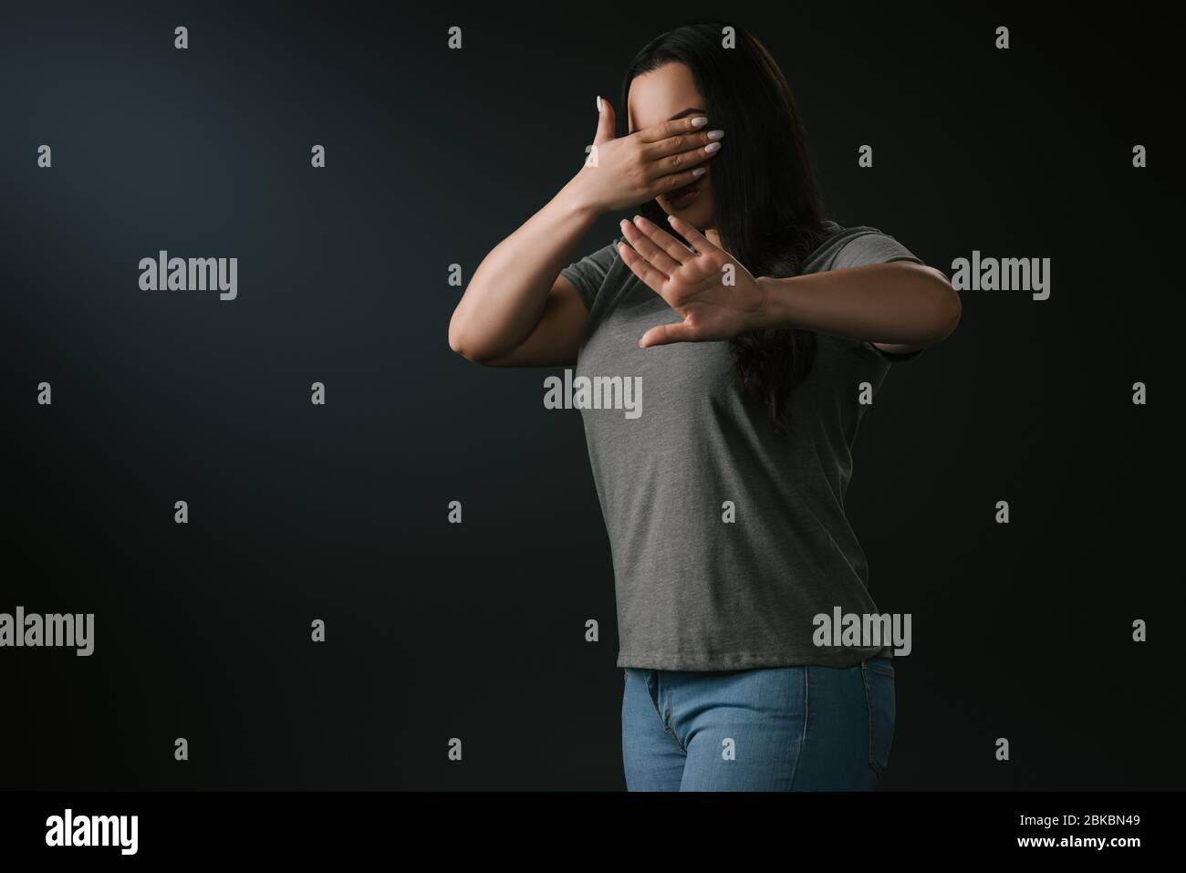 Plus size girl expressing blindness and denial with stop gesture isolated on black Stock Photo