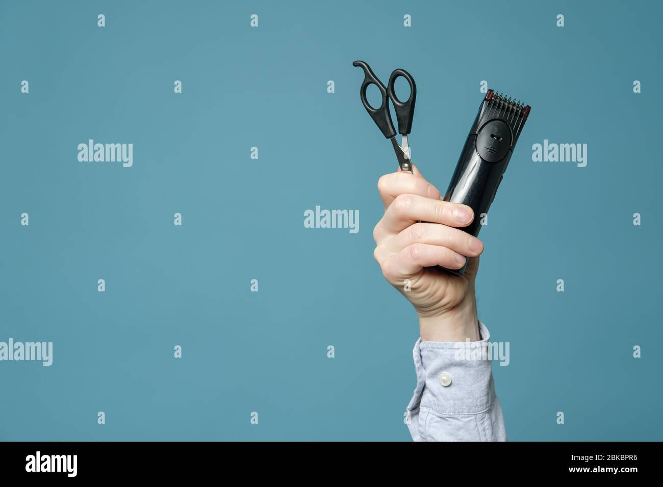 Male hand holds a hairdressing scissors and cordless trimmer. Studio, blue background. Copy space. Stock Photo