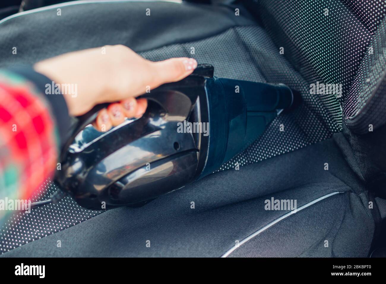 Driver cleans car with small vacuum cleaner. Woman takes care of auto