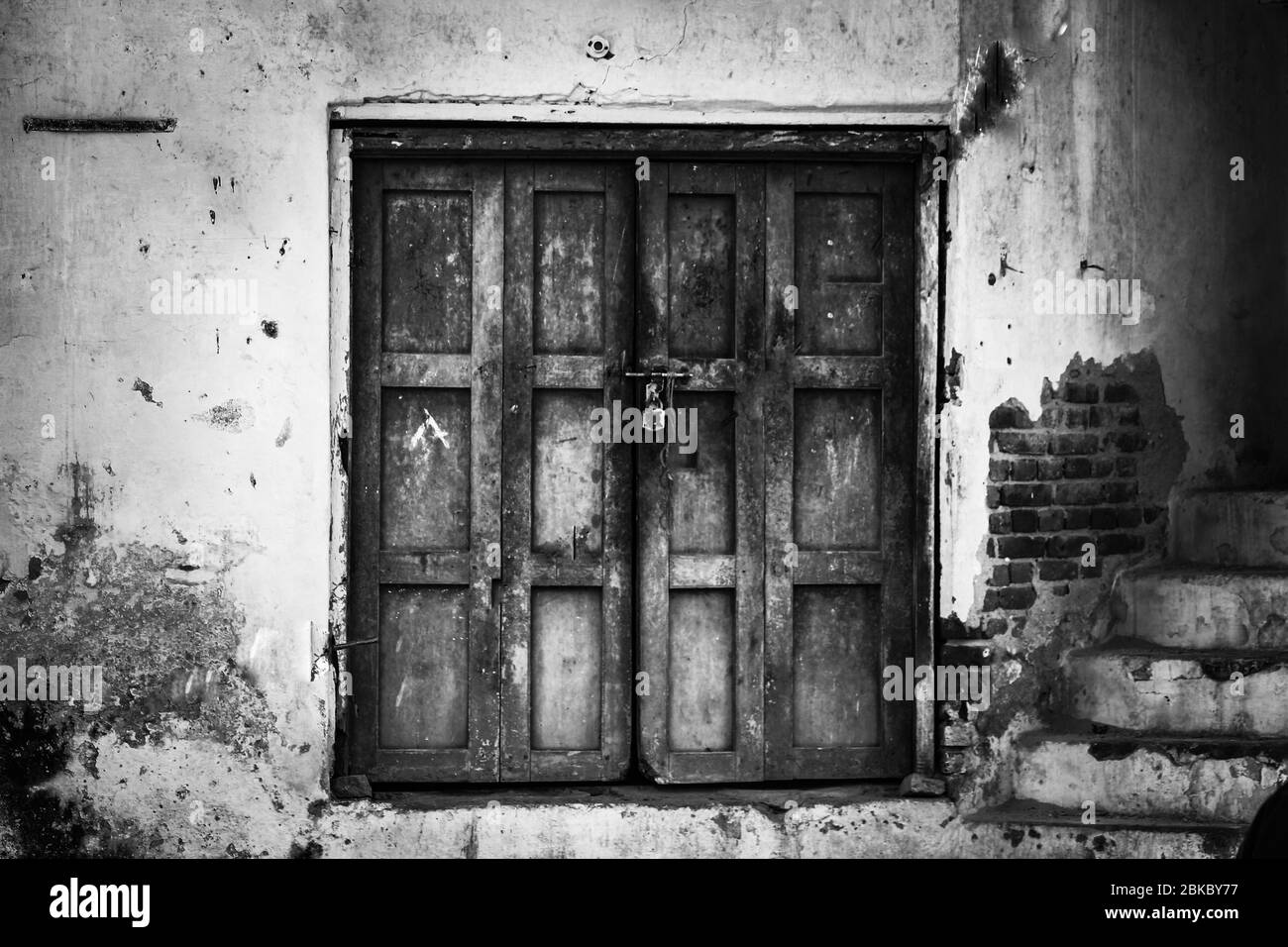 A monochrome picture of a closed home with a rustic wooden door Stock Photo